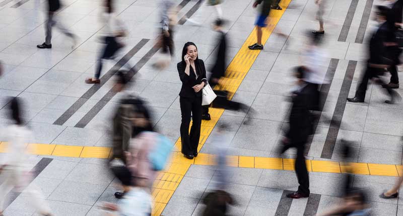 A Japanese woman talking on a mobile phone surrounded by commuters in an open area